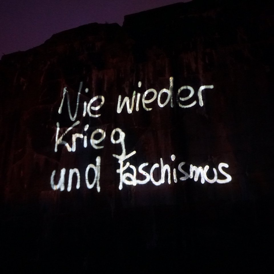 Erleuchtete Schrift auf dunkler Projektionfläche: Nie wieder Krieg und Faschismus